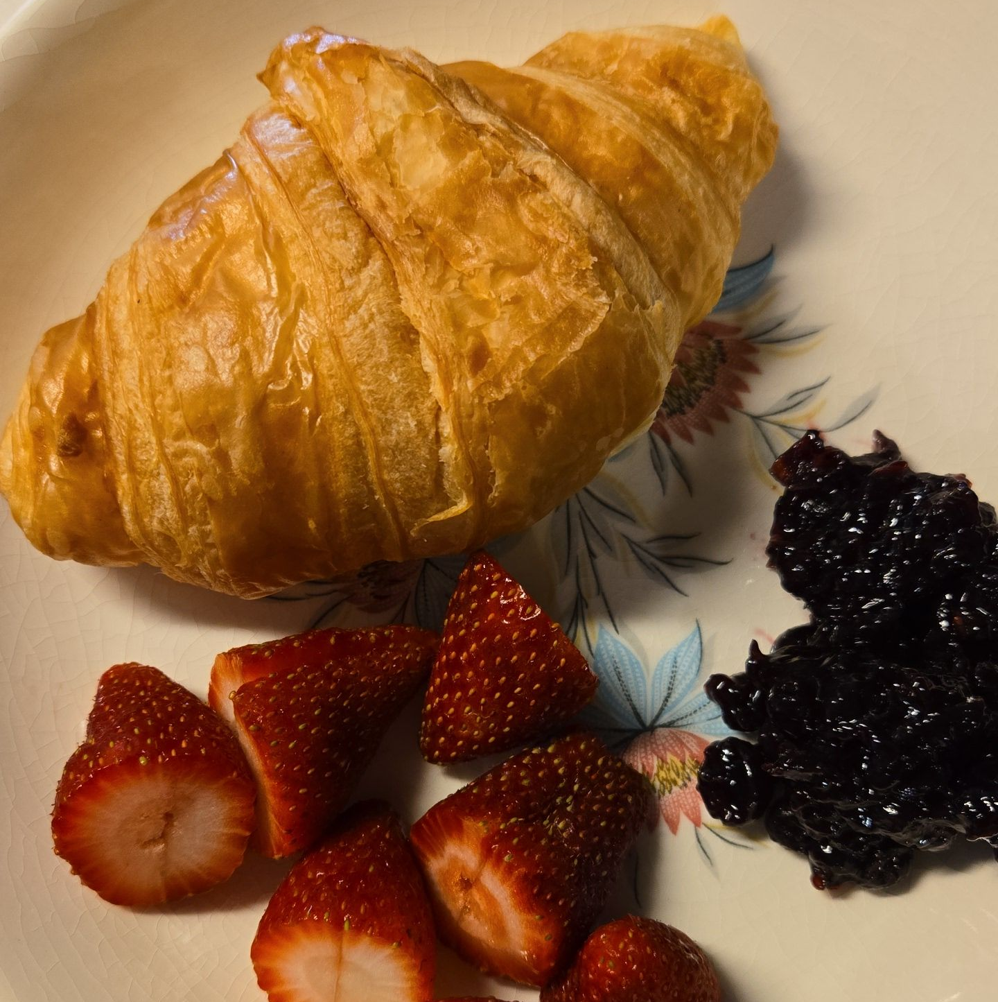 Un croissant, des fraises et de la confiture sur une assiette blanche.
