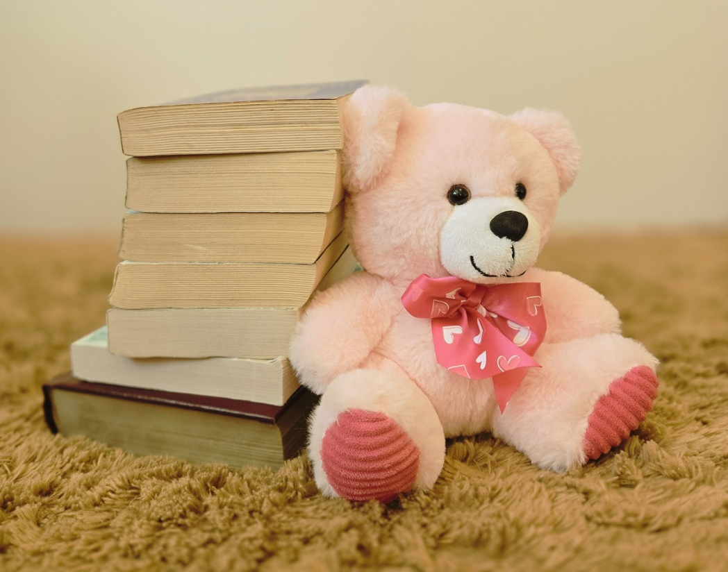 Pile de livres sur un lit avec un ourson rose